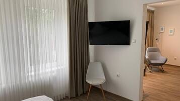 Ein modernes Hotelzimmer mit einem Bett, einem flachbildfernseher an der Wand, einem weißen Stuhl und Holzboden.
