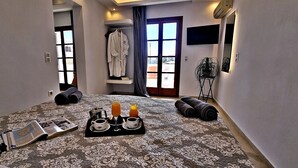 Hotelkamer met een groot bed, een klein tafeltje met ontbijtartikelen, een badjas aan een rek, en uitzicht naar buiten door een deur.