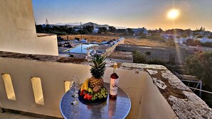 Een balkon met een tafel gedekt voor een drankje en fruit, met uitzicht op een zwembad en een bergachtig landschap.