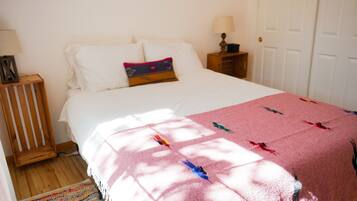 Un dormitorio con cama, almohadas, manta, mesita de noche, lámpara y una puerta.