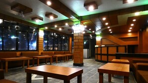 A modern interior with wooden furniture, a central pillar, and large windows. - Babai Resort (Thakudwara)