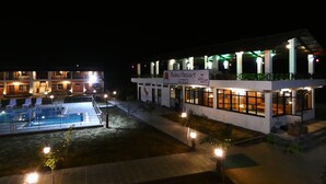 A hotel with a pool area, multiple floors, and outdoor lighting. - Babai Resort (Thakudwara)