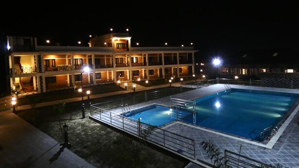 A hotel with a swimming pool, multiple balconies, and outdoor lighting. - Babai Resort (Thakudwara)