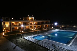 A hotel with a swimming pool, multiple balconies, and outdoor lighting. - Babai Resort (Thakudwara)