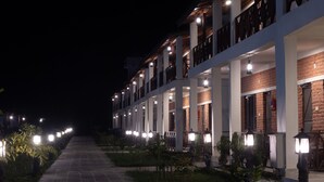 A multi-story hotel with a brick facade, multiple balconies, and a well-lit exterior walkway. - Babai Resort (Thakudwara)