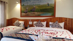 A hotel room with two beds, a wooden headboard, patterned pillows, and a painting of birds on the wall. - Babai Resort (Thakudwara)