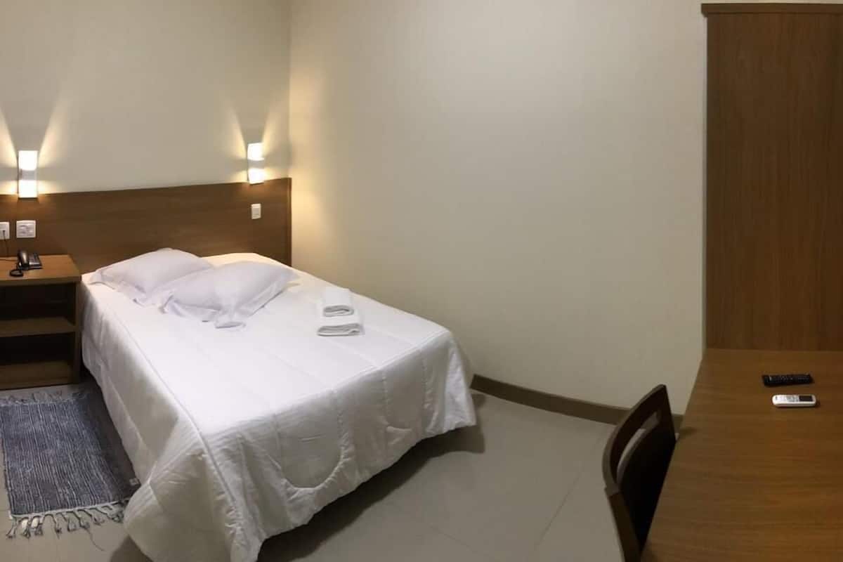 Hotelkamer met een bed, nachtkastje met telefoon, bureau met stoel en een airconditioner aan de muur.