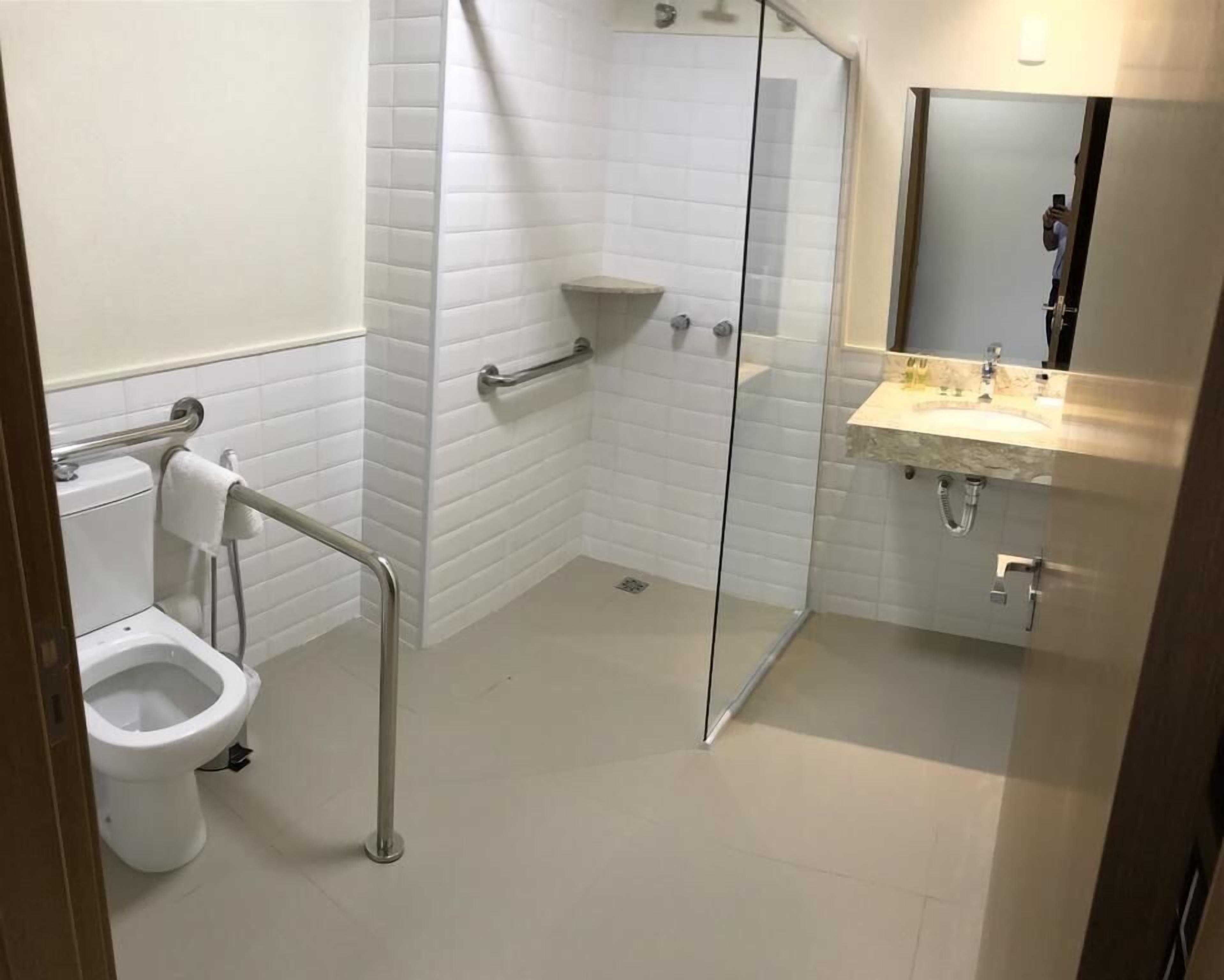 A modern bathroom with a glass shower enclosure, a white toilet with a grab bar, and a sink with a mirror.