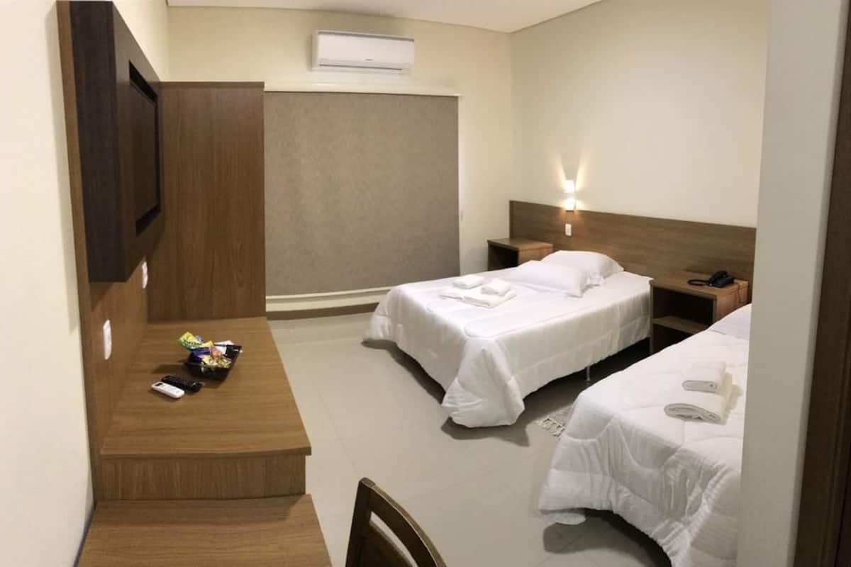 Een hotelkamer met twee bedden, een bureau met stoel, een aan de muur bevestigde televisie en een nachtkastje met lamp.