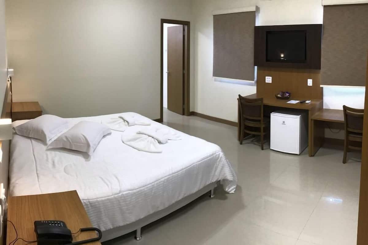 Een hotelkamer met een bed, een bureau, een stoel, een televisie en een kleine koelkast.