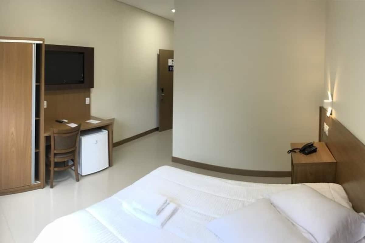 Een hotelkamer met een bed, een bureau, een televisie, een kledingkast en een nachtkastje.