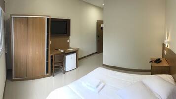 Una habitación de hotel con cama, escritorio, televisión, armario y mesita de noche.