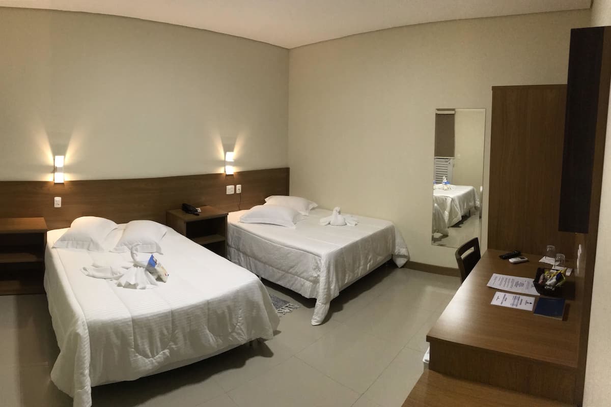 Een hotelkamer met twee bedden, een houten hoofdbord, nachtkastjes, een spiegel, een bureau met stoel, en een tafeltje met spullen erop.