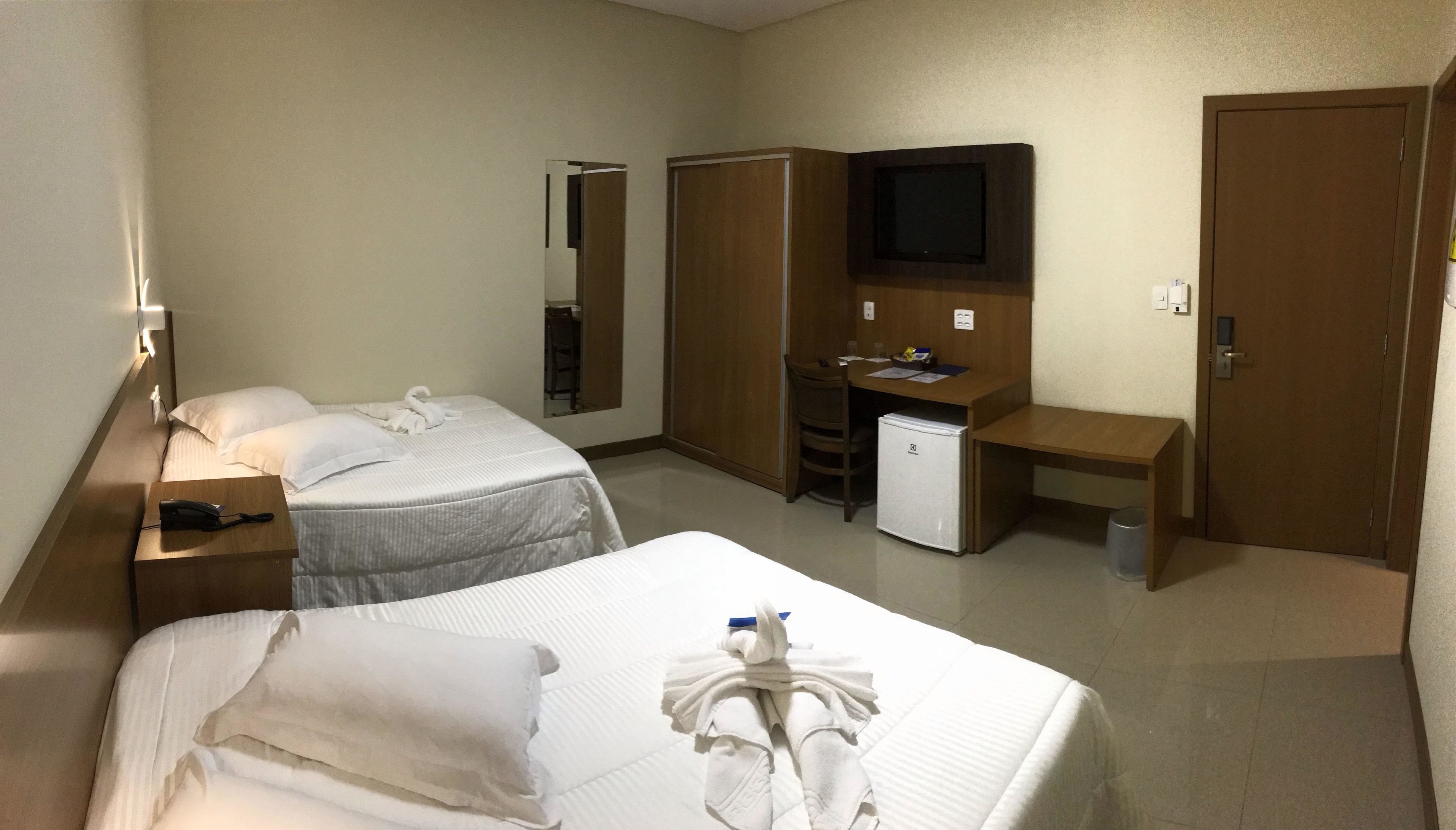 A hotel room with two beds, a desk, a television, and a wardrobe.