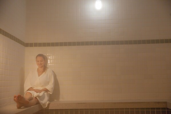 A person sitting in a bathtub with tiled walls and a light fixture above.
