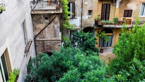 A narrow courtyard with a mix of old and new buildings, featuring balconies with plants and a small archway. - A World Aparts - Torre Argentina Apartments (Rome)