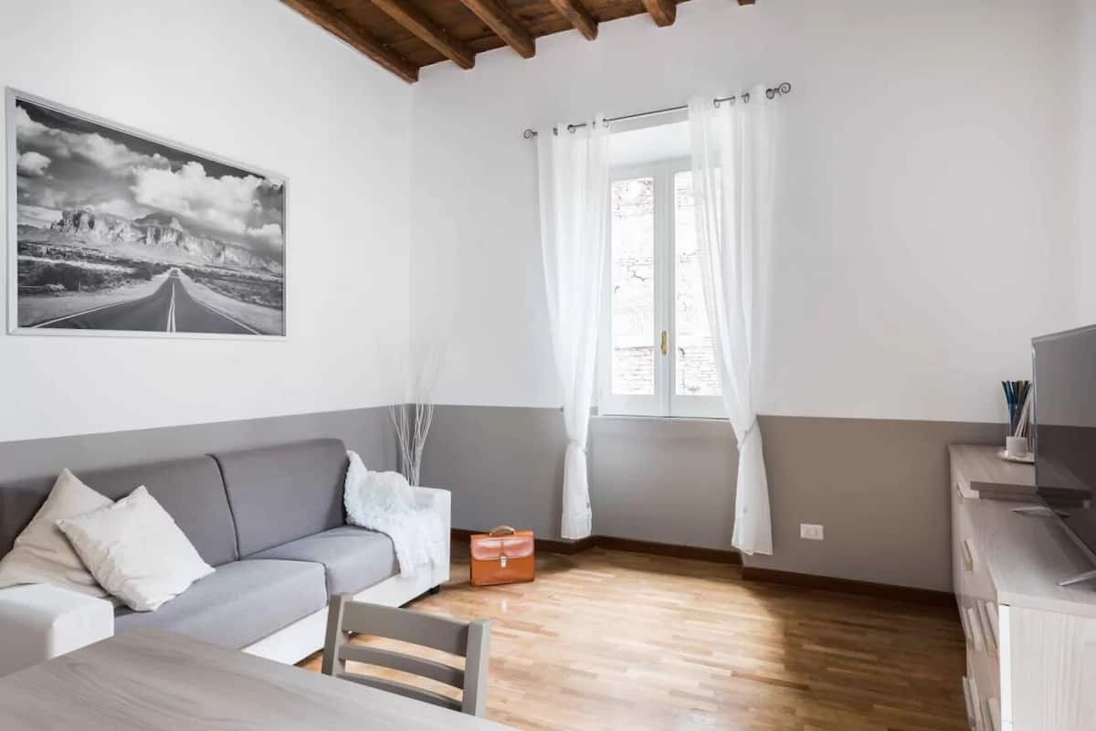 Un salon moderne avec un canapé gris, une table à manger en bois et une grande fenêtre ornée de rideaux blancs.