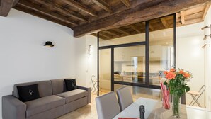 A modern living room with a grey sofa, a dining table with chairs, a vase with flowers, and a bottle of wine. - A World Aparts - Torre Argentina Apartments (Rome)