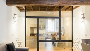 A modern kitchen with a glass partition, wooden ceiling beams, and a sofa with a pillow in a living area. - A World Aparts - Torre Argentina Apartments (Rome)