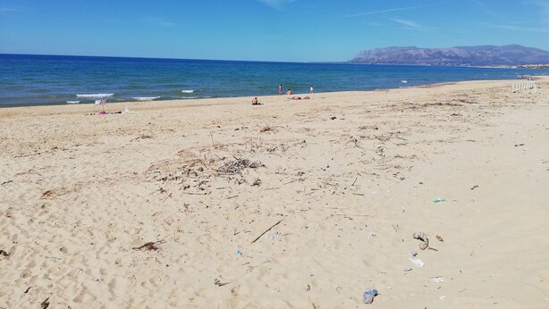 Ein Strand mit Sand, Meer und Bergen im Hintergrund.