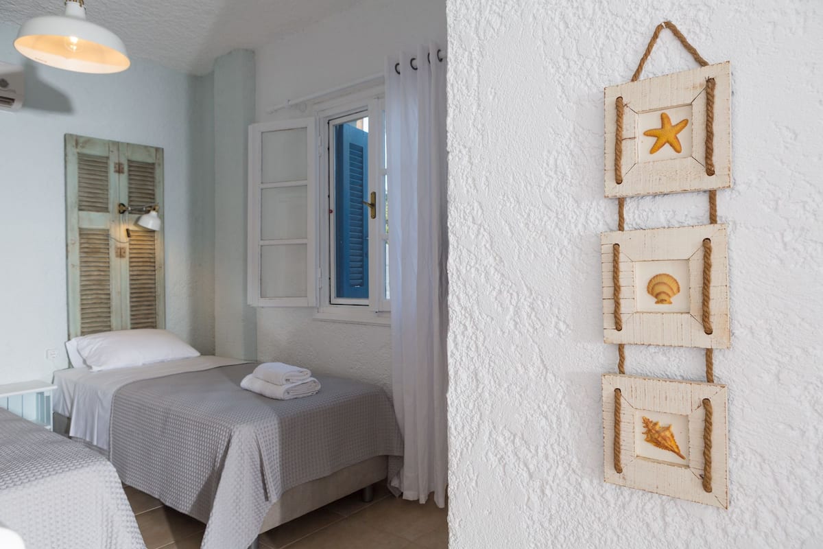 Ein Schlafzimmer mit zwei Betten, einem Fenster mit blauen Rollläden und einer Wanddekoration mit Seesternen und Muscheln.