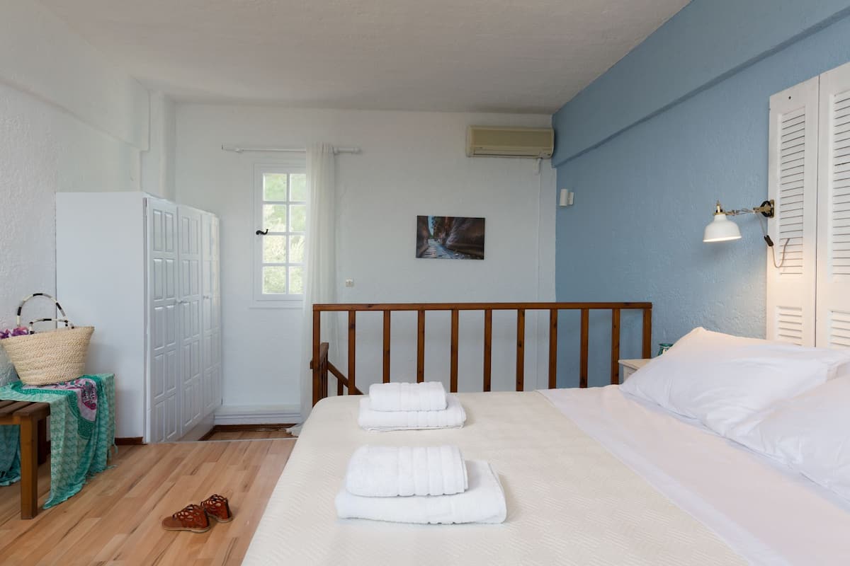 Ein Schlafzimmer mit einem hölzernen Kopfende, einem Bett mit weißer Bettwäsche, einem Holzboden, einem weißen Kleiderschrank, einem kleinen Tisch mit einem Korb und einem Bild an der Wand.
