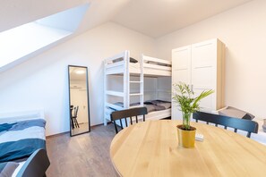 Ein Schlafsaalzimmer mit Etagenbetten, einem runden Holztisch, einem Blumentopf und einem Spiegel.