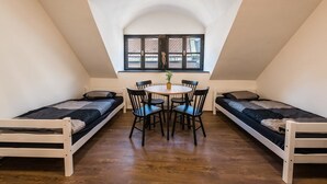 A dormitory room with two single beds, a round table with chairs, and a window with shutters. - Apart-Hostel ZERO (Bratislava)