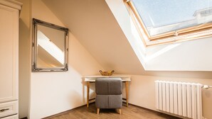 A small, well-lit attic bedroom with a sloped ceiling, a large mirror, a white desk with a basket, and a radiator. - Apart-Hostel ZERO (Bratislava)