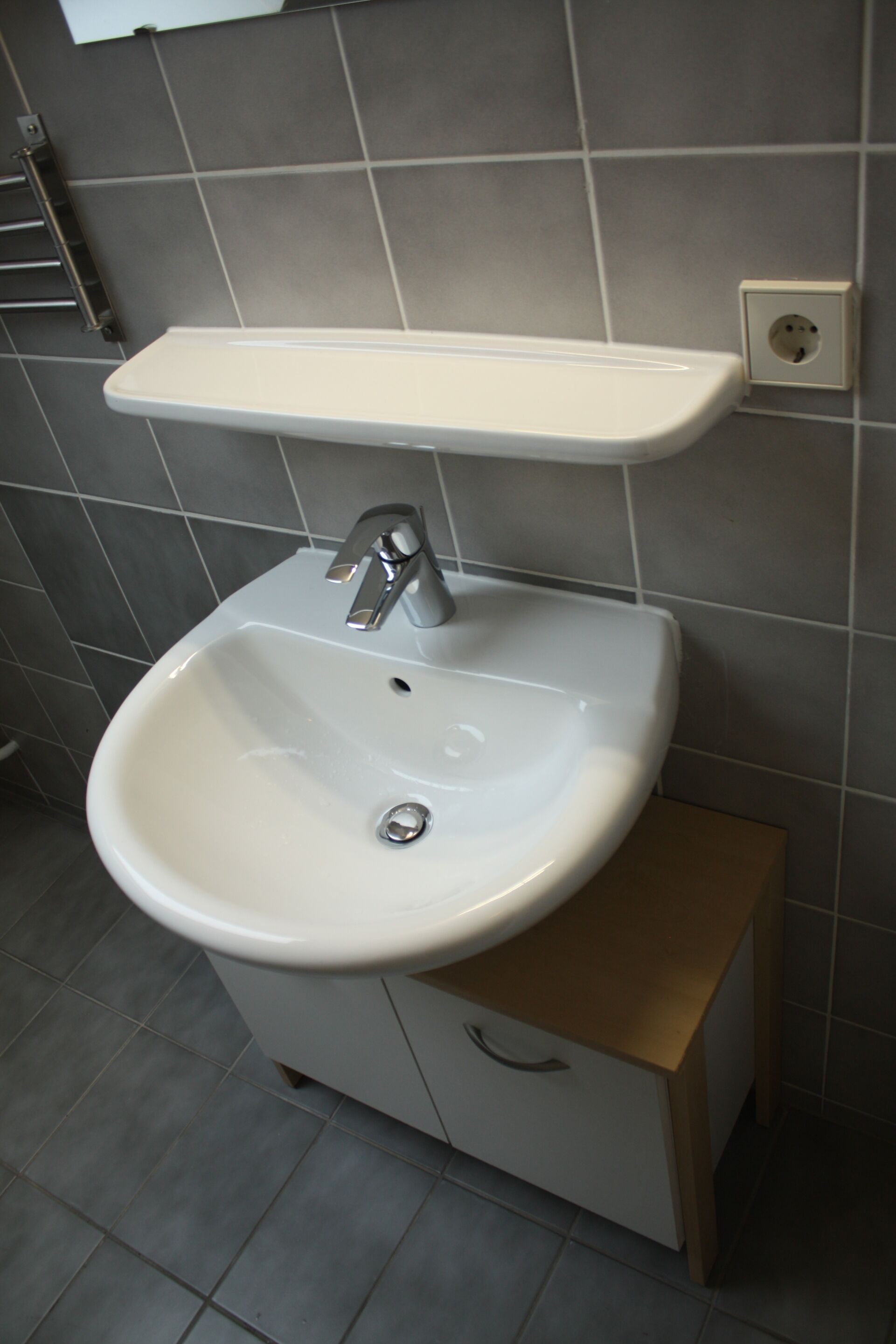 A bathroom with a white sink, a mirror above it, and a towel rack to the left.