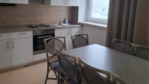 Una cocina compacta con armarios blancos, estufa y mesa de comedor con sillas de mimbre.