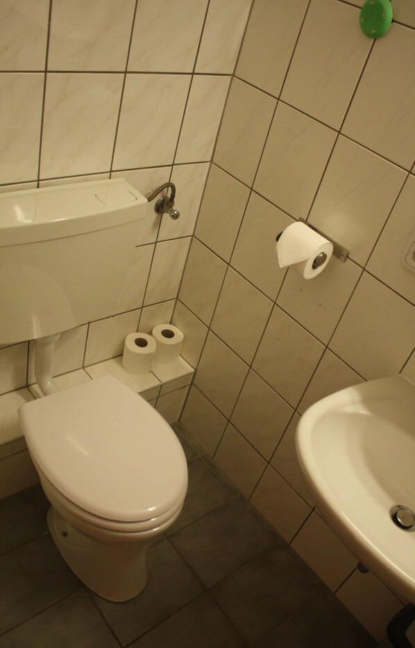 A bathroom with a toilet, two rolls of toilet paper, a sink, and a green bottle on the wall.