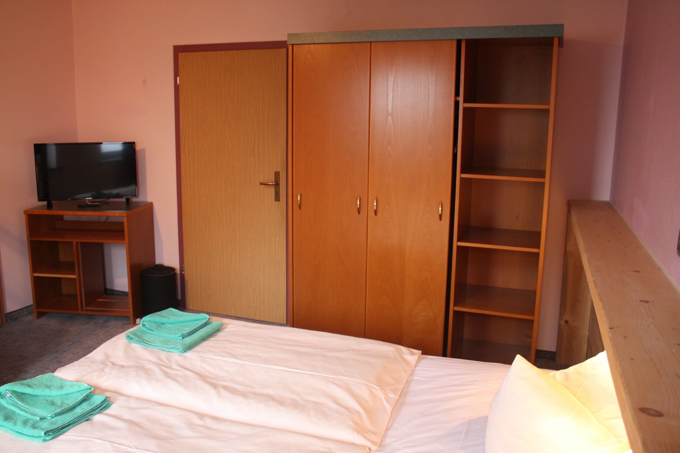 A bedroom with a bed, a TV on a stand, a wardrobe, and a shelf unit.