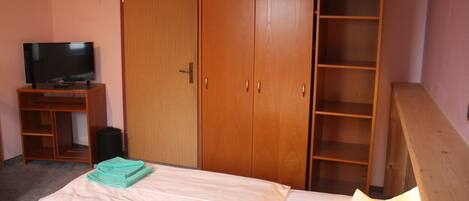 A bedroom with a bed, a TV on a stand, a wardrobe, and a shelf unit.