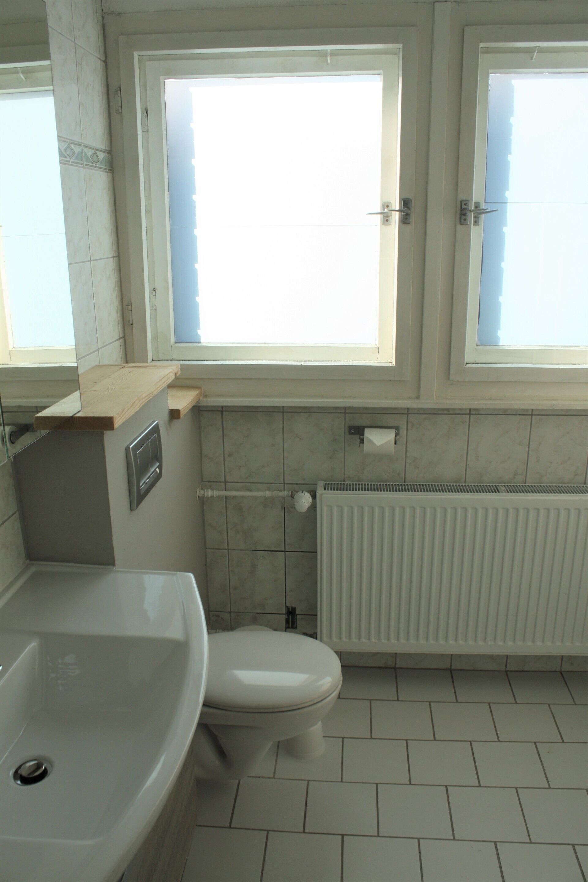 A bathroom with a white sink, toilet, and a window above the toilet.