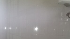 A small, tiled bathroom with a toilet, a visible pipe, and a wall-mounted fixture above the toilet. - Trust White Hotel (Bushenyi)