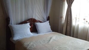 A bed with a wooden headboard, white pillows, and a beige blanket. - Trust White Hotel (Bushenyi)