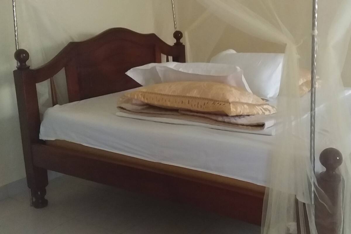 A bed with a wooden frame, white bedding, and a beige pillow.