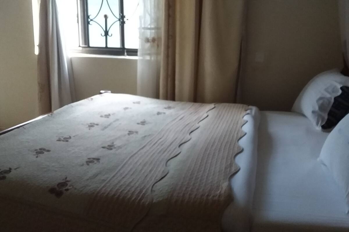 A bed with a floral bedspread, a wooden headboard, and a window with curtains.