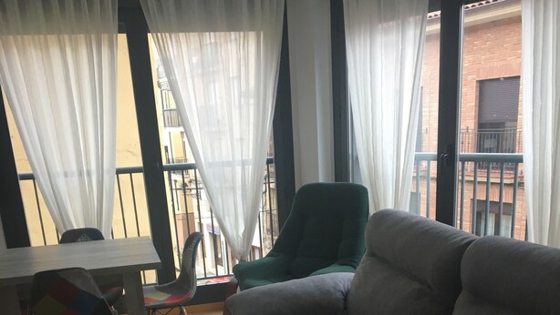 Un salon avec un canapé gris, une table basse en bois, un fauteuil vert et une table à manger avec des chaises.