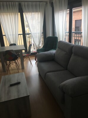 A living room with a grey sofa, a wooden coffee table, a green armchair, and a dining table with chairs.