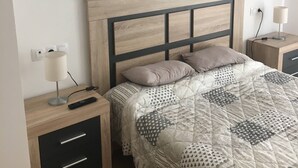 Une chambre à coucher avec une tête de lit en bois, un lit recouvert d’une literie à motifs, des tables de chevet avec des lampes et une commode.