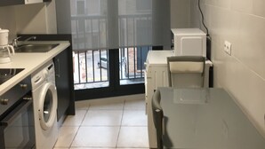 Une cuisine compacte équipée d’un lave-linge, d’une petite table et d’une chaise. Une fenêtre donne sur l’extérieur et offre une vue.
