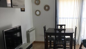 Un salon moderne avec un téléviseur, des meubles en bois, une table à manger et une grande fenêtre avec des rideaux.