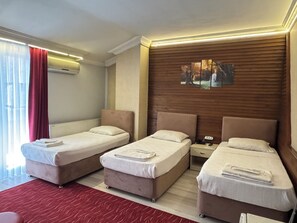 Habitación de hotel con dos camas individuales, una mesita de noche, alfombra roja y una ventana con cortinas.