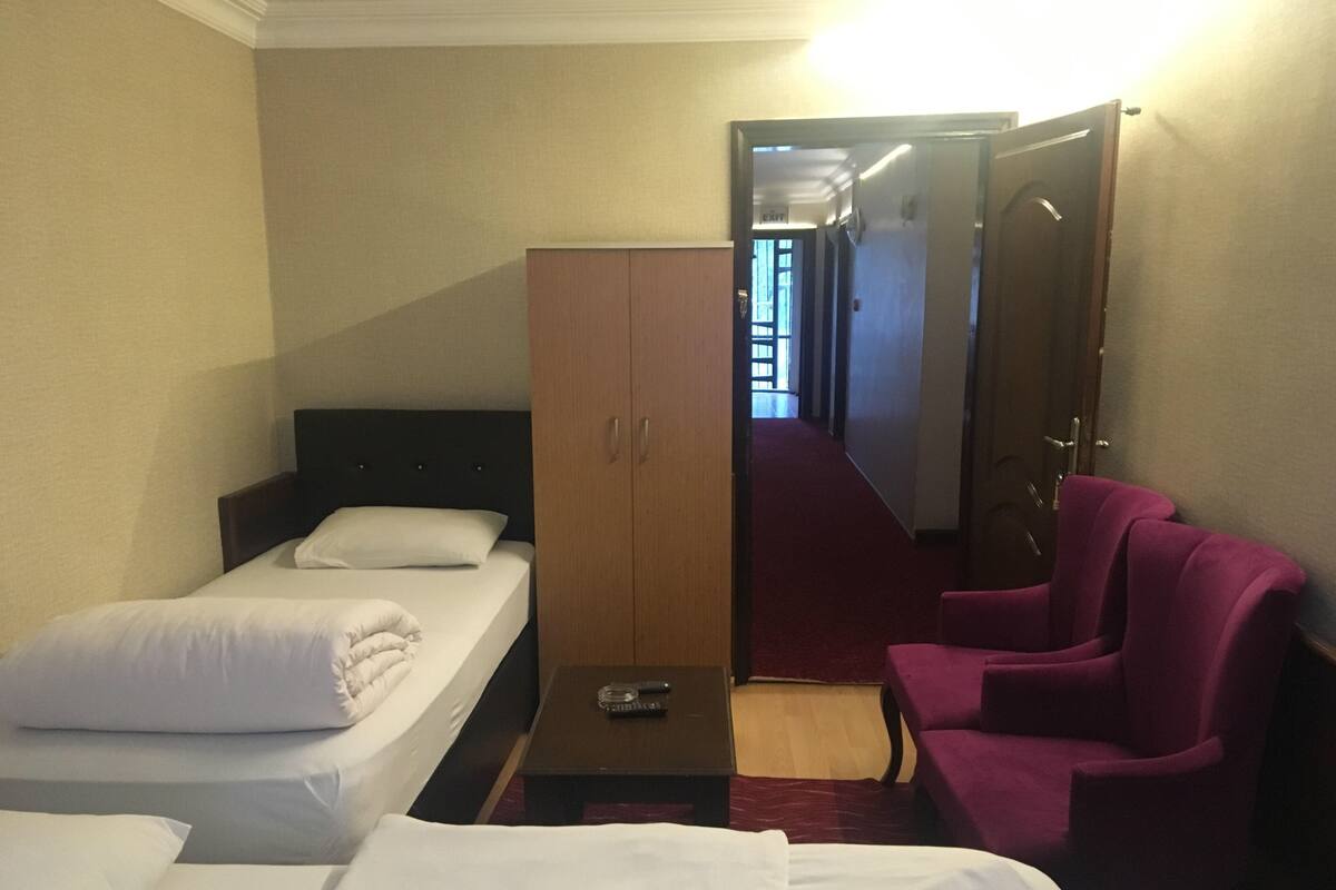 A hotel room with two single beds, a wooden wardrobe, a small table, and a purple armchair.