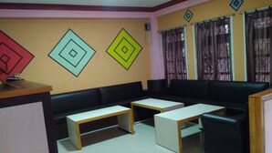 A room with a black sofa, two white tables, and a wooden counter. - Big Bell Guest House (Bhaktapur)