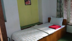 A small, single-bed room with a wooden headboard, a green carpet, and a window with curtains. - Big Bell Guest House (Bhaktapur)