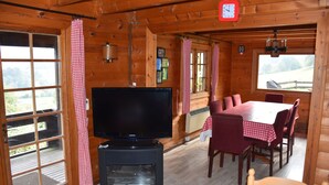 A wooden cabin interior with a TV on a stand, a dining table with chairs, and a large window. - Scandinavian chalet, warm atmosphere, for those who love nature (Lierneux)