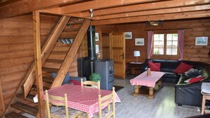A wooden cabin interior with a dining table, chairs, a sofa, a fireplace, and a staircase. - Scandinavian chalet, warm atmosphere, for those who love nature (Lierneux)